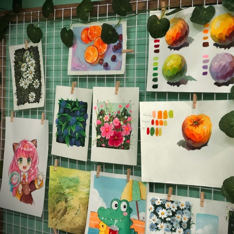 Một loạt tranh được treo trên lưới sắt, gồm nhiều chủ đề như hoa cúc, hoa hồng, trái cây, phong cảnh và nhân vật hoạt hình, tạo nên không gian nghệ thuật đa dạng và sinh động.